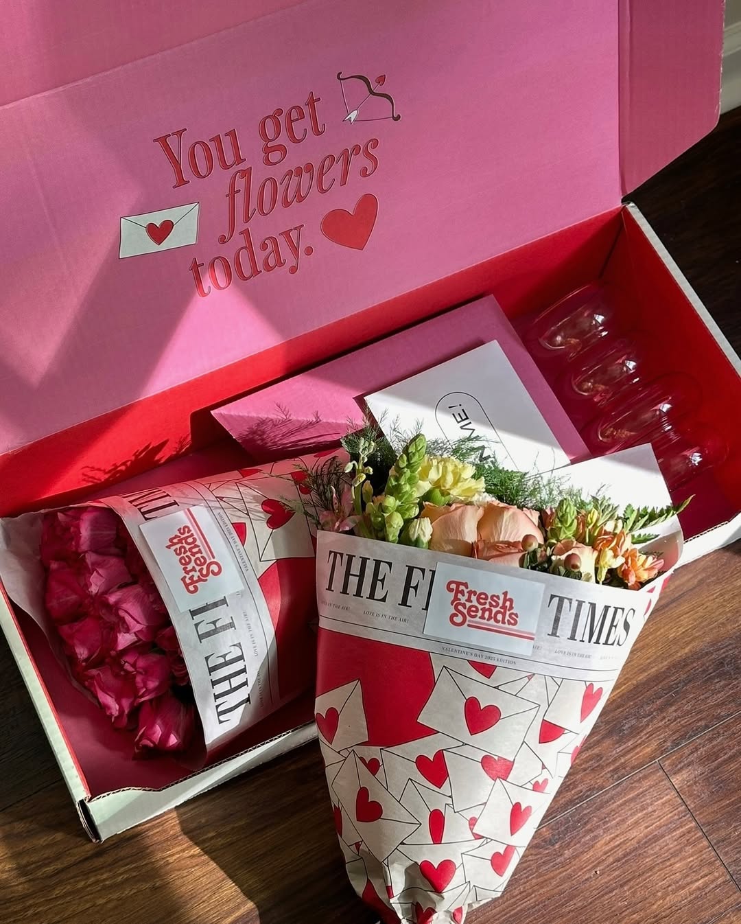 Open Fresh Sends’ mailer with two flower bouquets, a card, and glass vases on Valentine’s Day.-319594922351