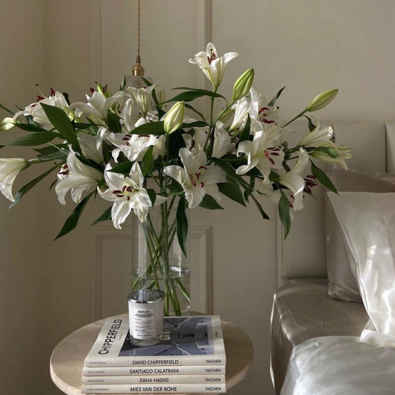 White lilies from Fresh Sends arranged in a clear vase on a side table, offering a calming and comforting presence for hospital patients.