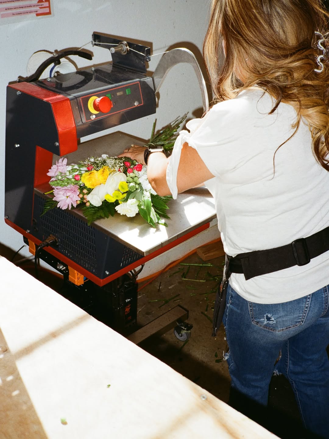 A woman with wavy brown hair arranging a colorful Fresh Sends bouquet on a wrapping machine.-318484054383