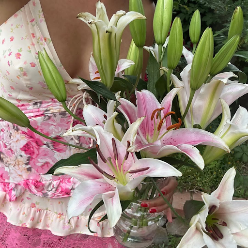 Woman in floral dress holding pink and white lilies in a clear vase, gift arrangement from Fresh Sends.-317399499119