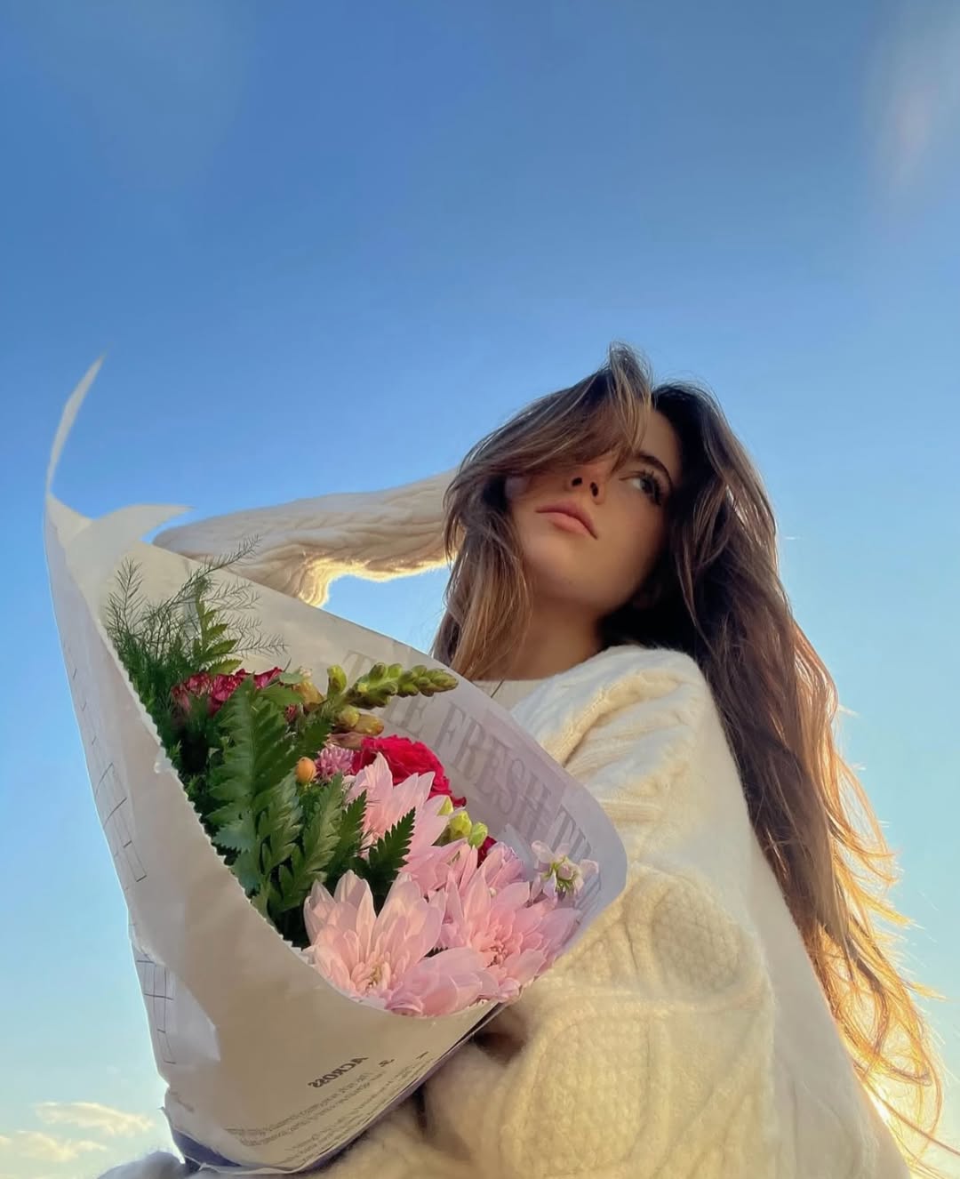 Woman holding a Fresh Sends bouquet of pink and red flowers outdoors under a bright blue sky.-321112965487