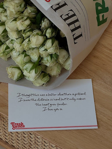 A bouquet of white roses from Fresh Sends with a handwritten note that reads, “I thought this was better than a postcard. I know the distance is hard but it only makes the heart grow fonder. I love you so.”