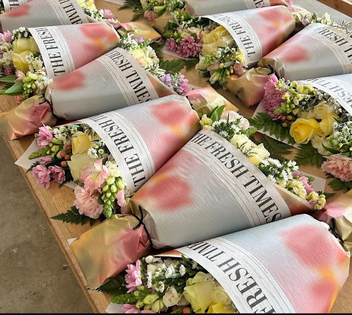 Row of Fresh Sends bouquets wrapped in newspapers, arranged neatly together showcasing vibrant flowers.-318022910319