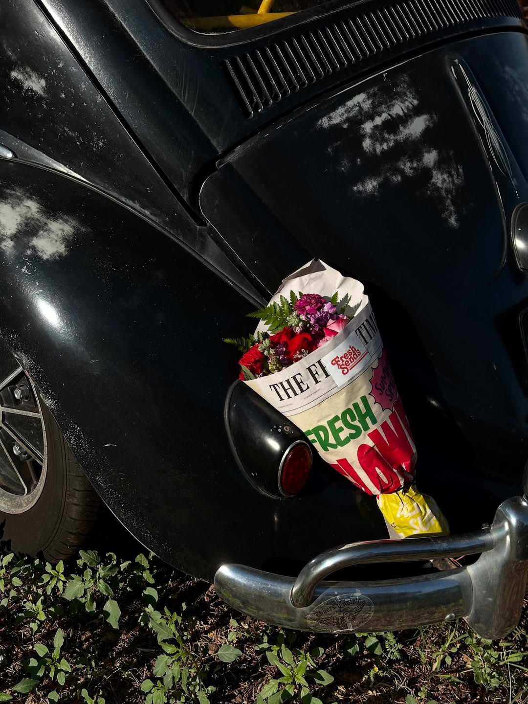 A Fresh Sends colorful bouquet wrapped in a newspaper-style wrap, resting on a black car.-319448351087