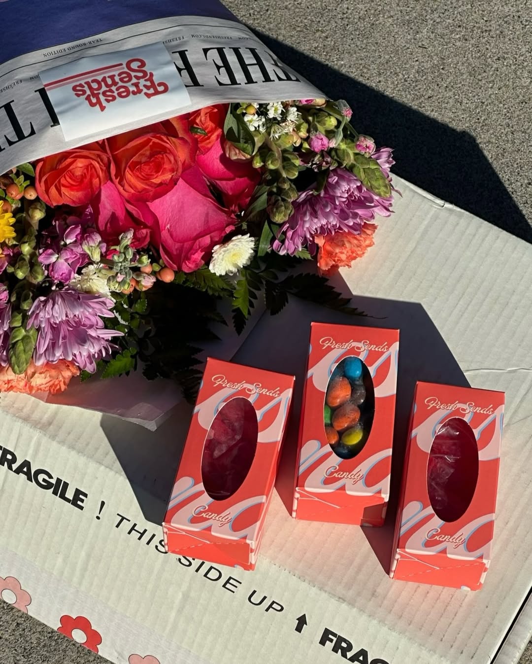 Colorful Fresh Sends bouquet beside three candy boxes arranged on a shipping box, showcasing thoughtful gifting.-317547184495