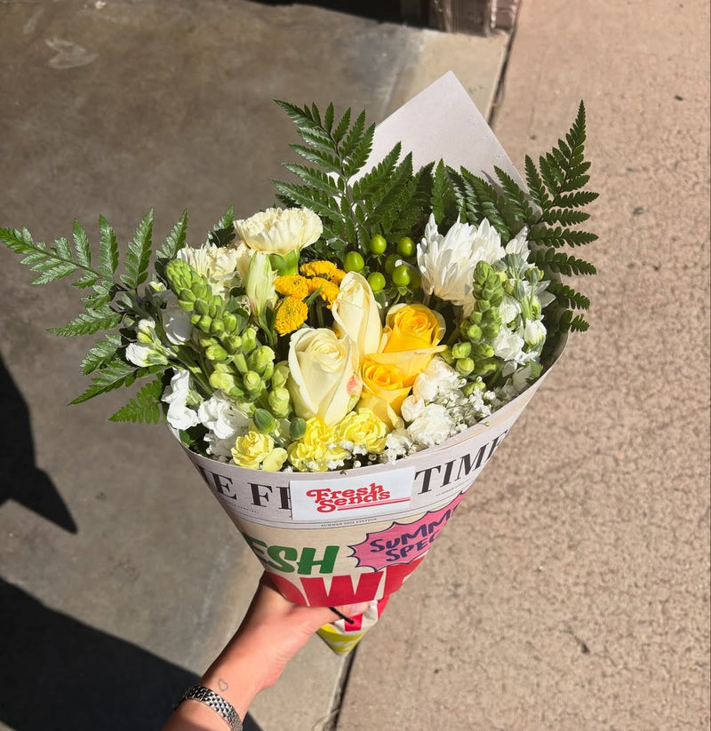 A person holding a Fresh Sends bouquet with yellow and cream flowers and greenery.