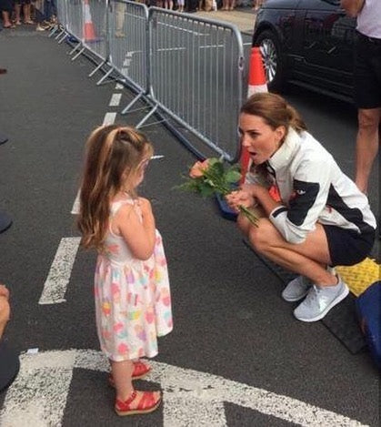 A mother kneels beside her daughter while holding a Fresh Sends flower bouquet outdoors.