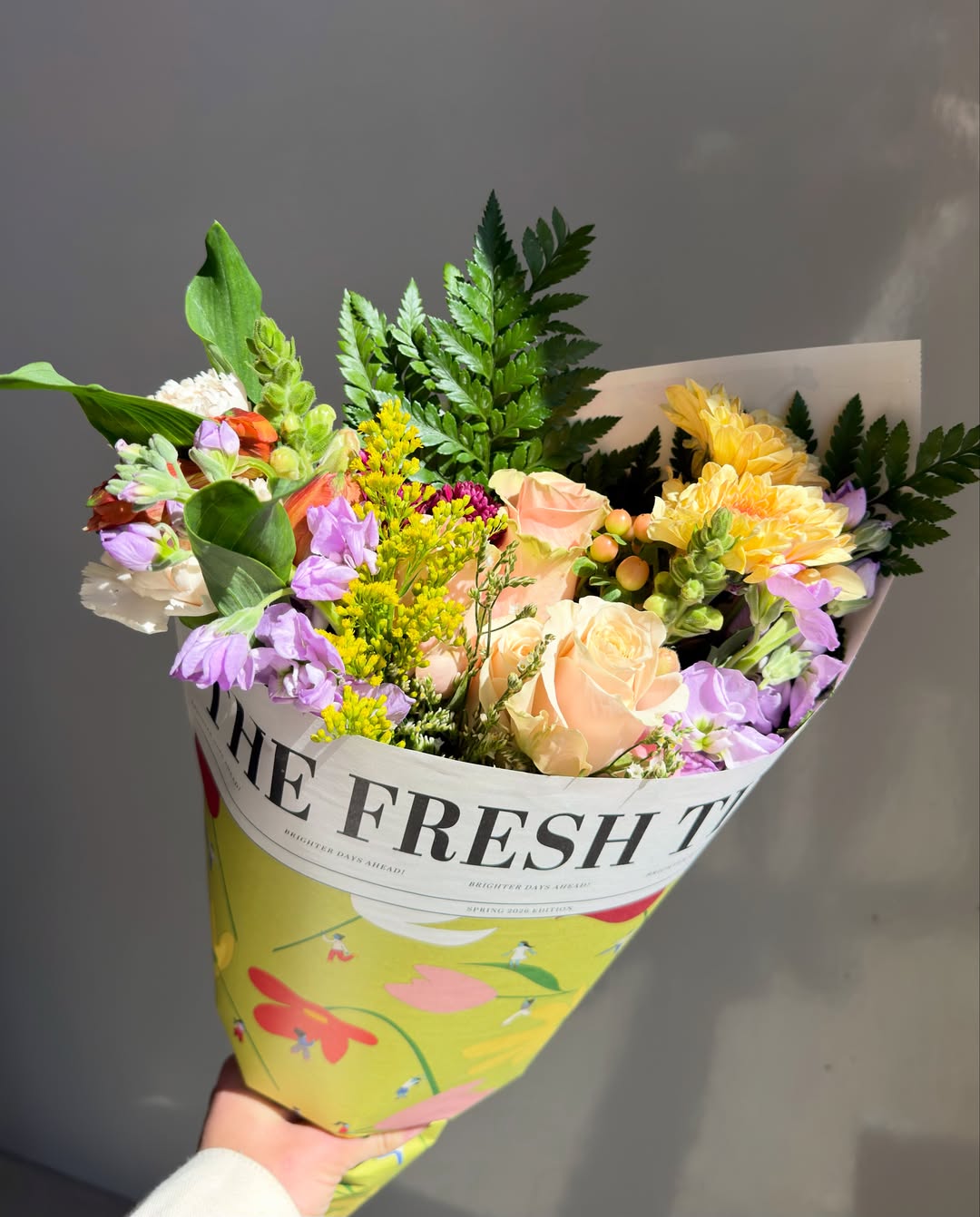 Fresh Sends bouquet wrapped in a newspaper-style floral sleeve featuring a colorful mix of seasonal blooms and greenery.-320990577007