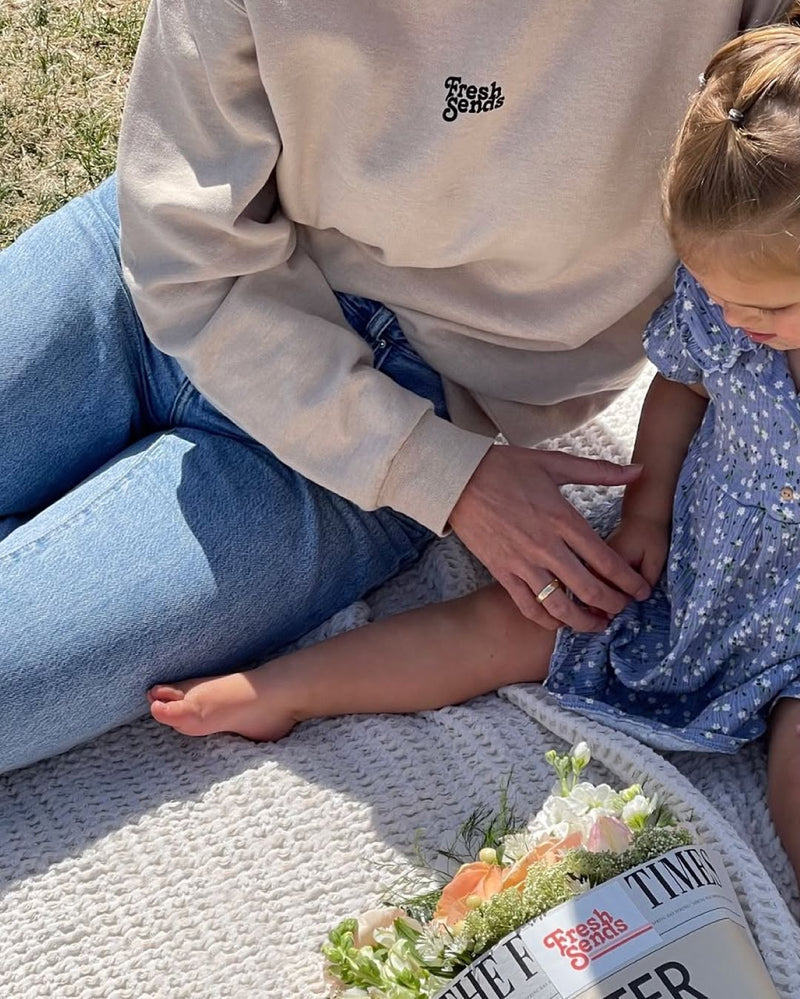 Mother and child sitting on a picnic blanket with a wrapped flower bouquet, sharing a relaxed outdoor moment.