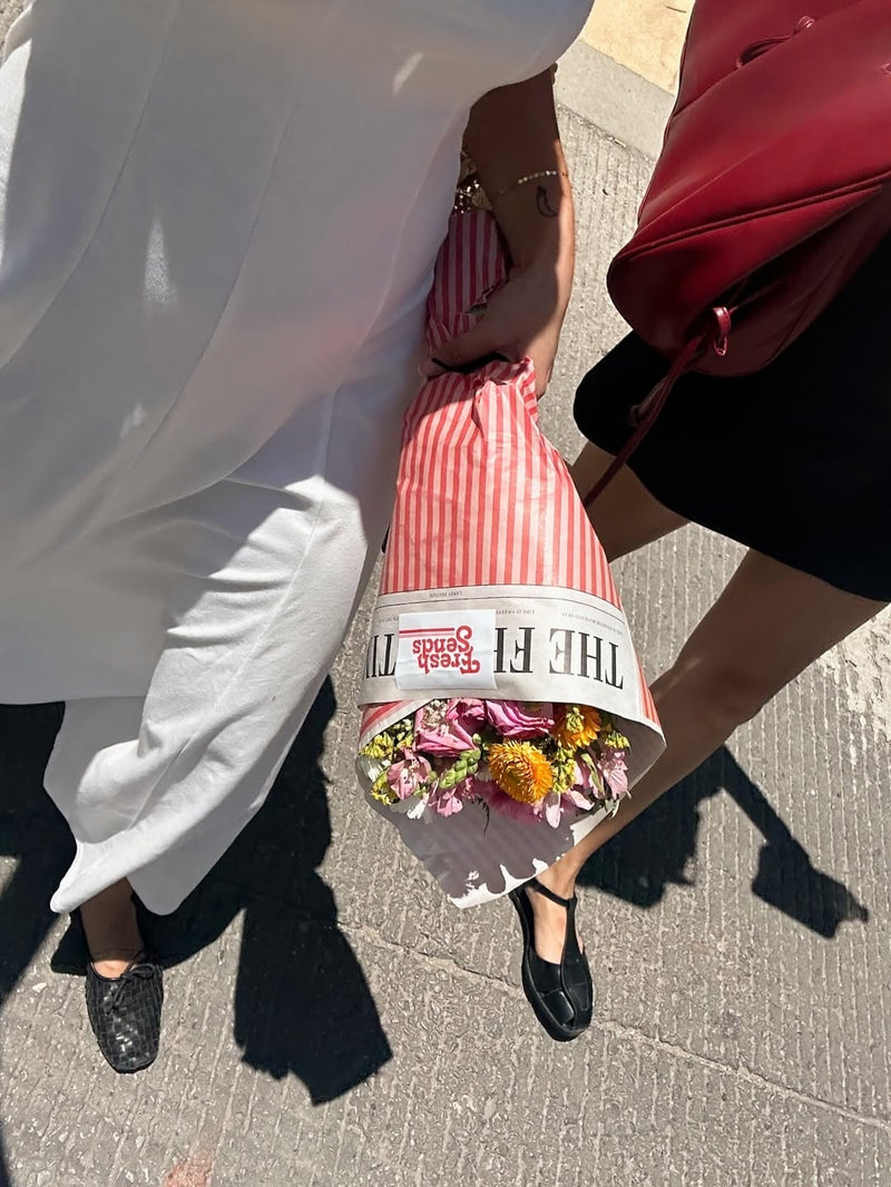 Two people walking outdoors, with one holding a Fresh Sends wrapped bouquet.