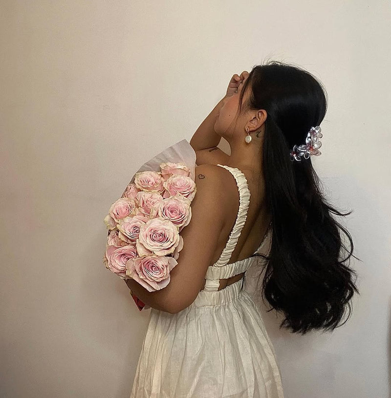 Person in a white dress holding a large bouquet of soft pink Fresh Sends roses while standing in profile outdoors.